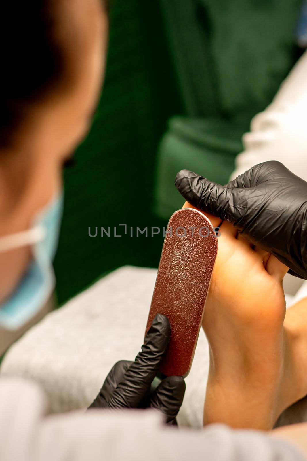 Pedicurist rubbing heel with a special grater on pedicure treatment in a beauty salon. by okskukuruza