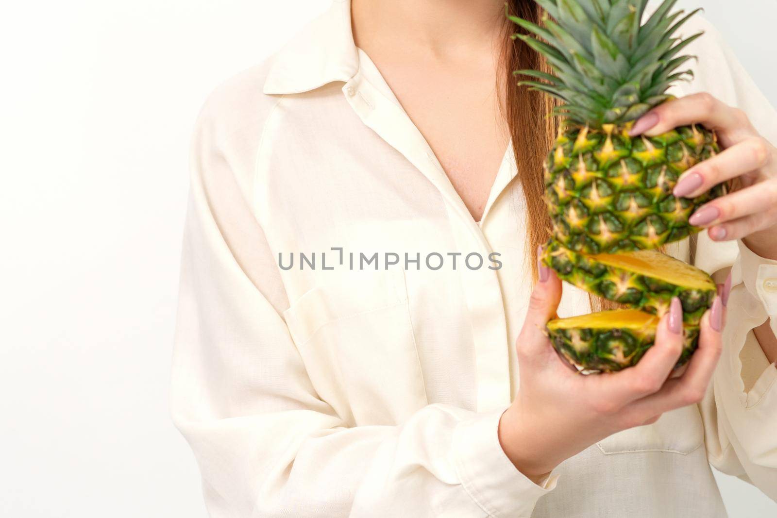 Beautiful young Caucasian woman holding pineapple and smiling, wearing a white shirt over white background. by okskukuruza