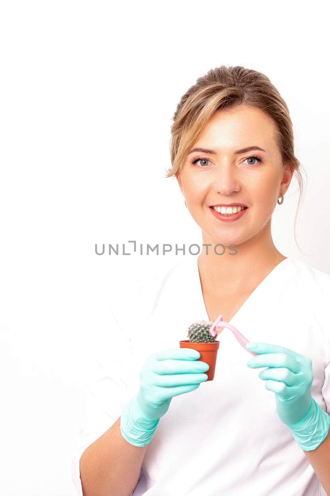 A smiling female beautician holds little green cactus with the razor in her hands. Hair removal concept