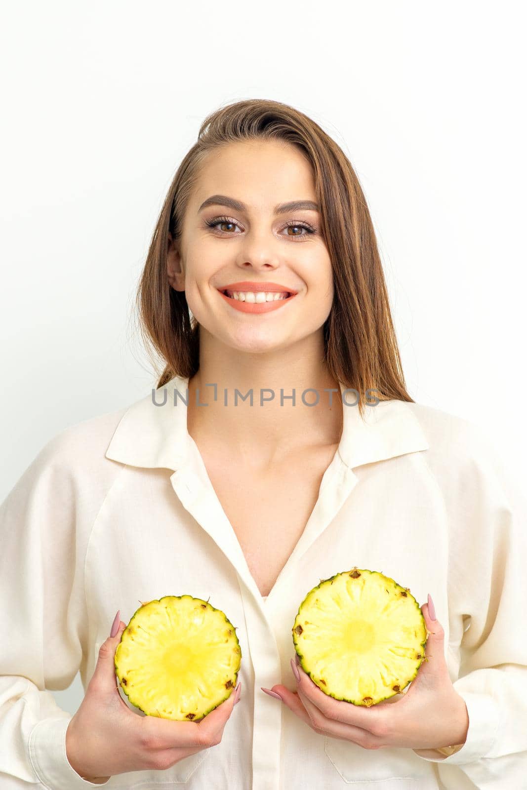 Young Caucasian smiling woman holding slices pineapple over white background, breast health concept. by okskukuruza