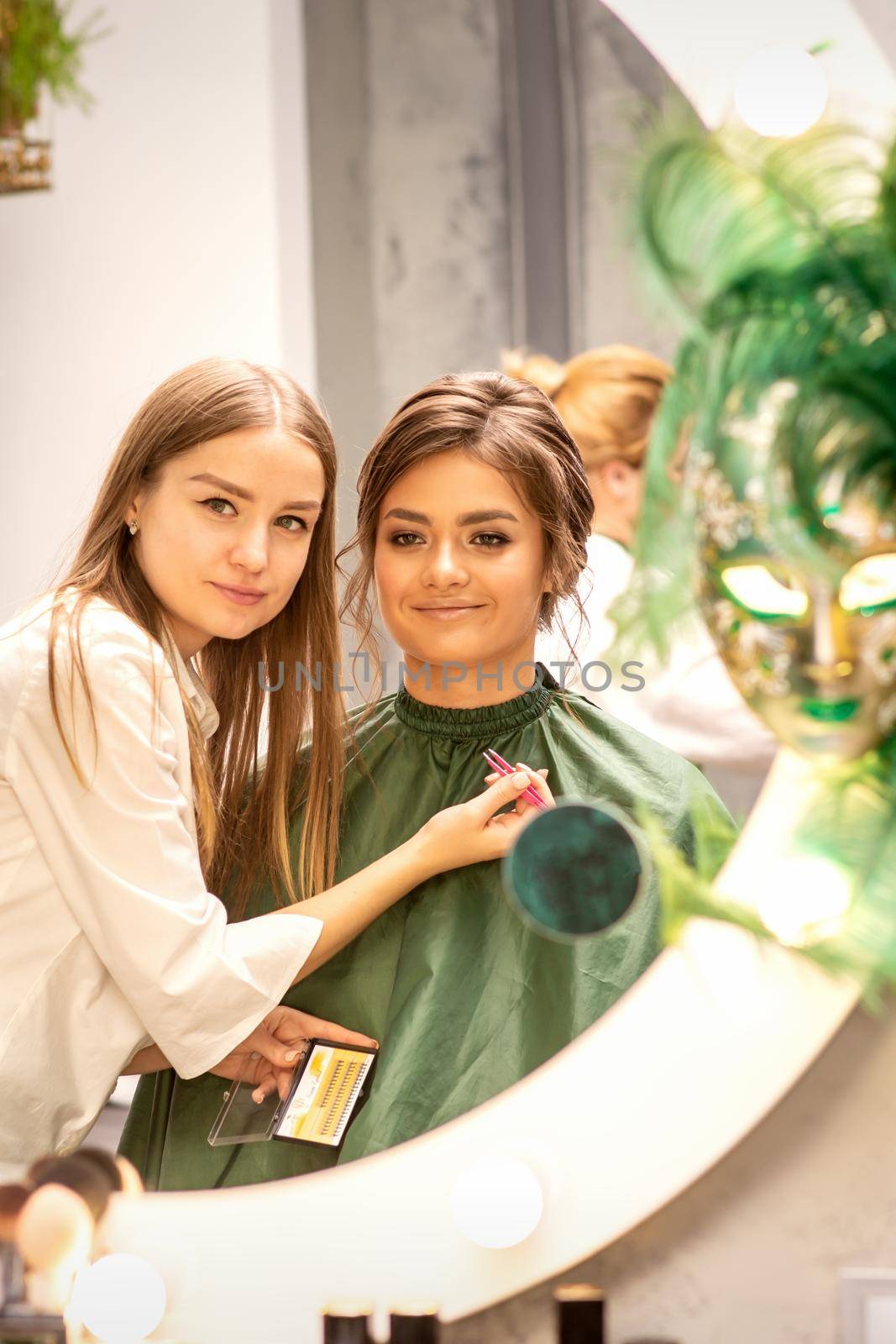 Professional make up artist and beautiful girl looking in the mirror smiling in a beauty salon