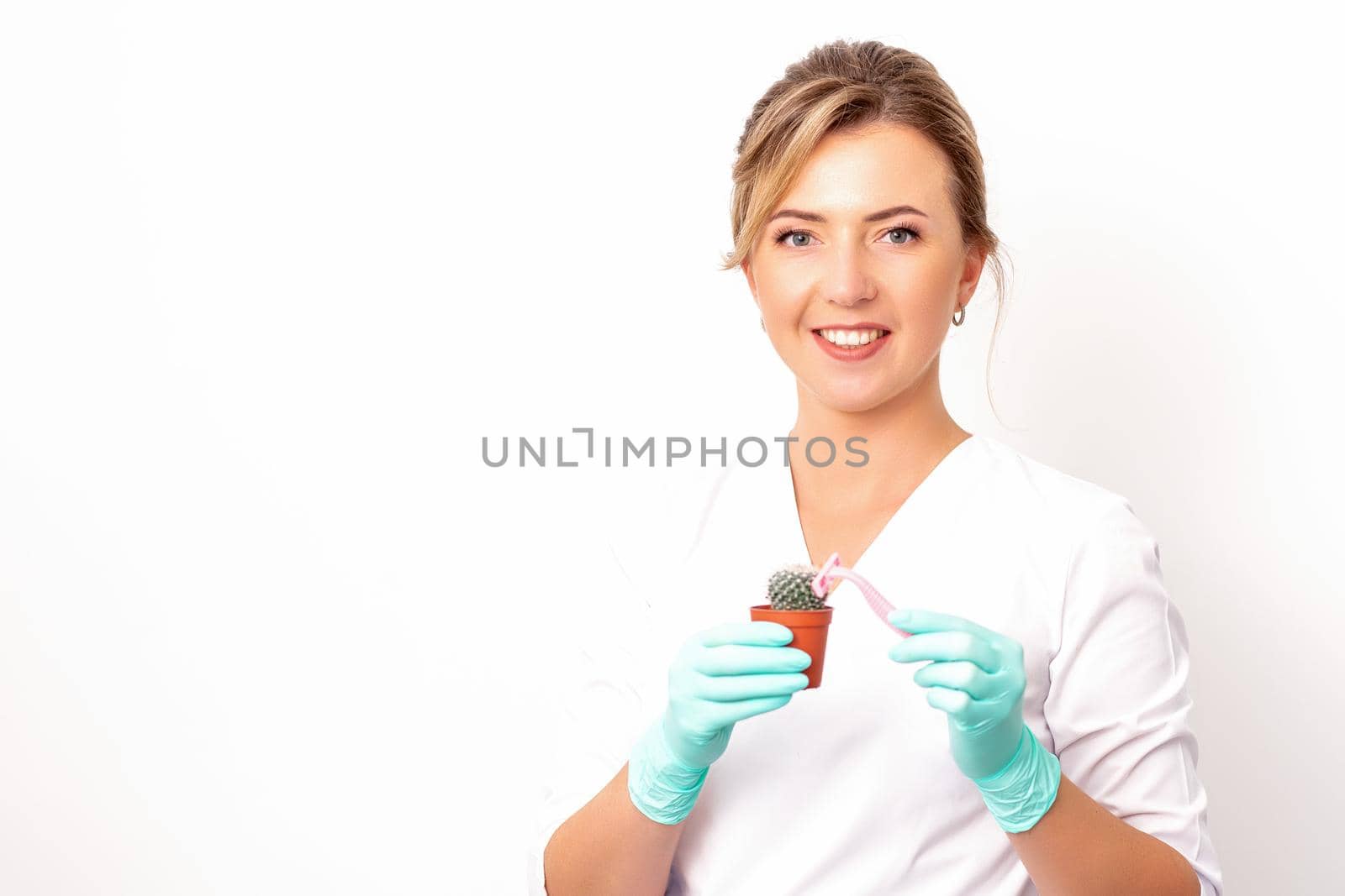 A smiling female beautician holds little green cactus with the razor in her hands. Hair removal concept