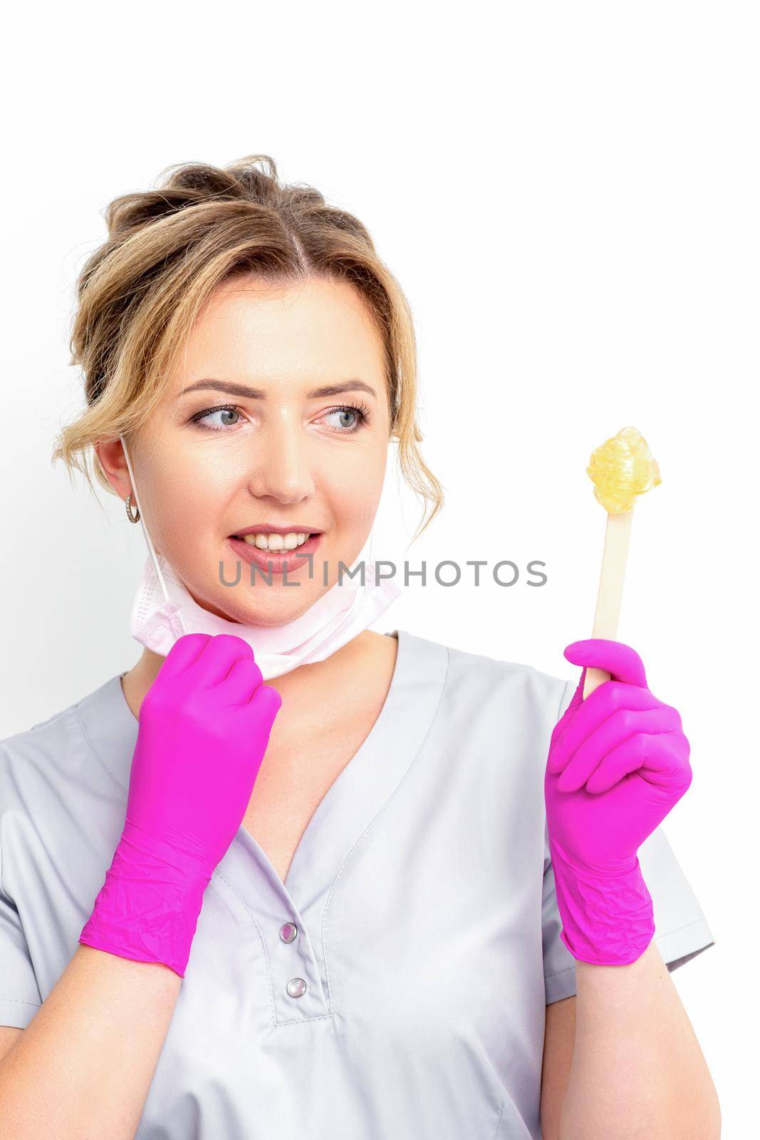 The master of sugar hair removal holds liquid yellow sugar paste, wax for depilation on a wooden stick on a white background