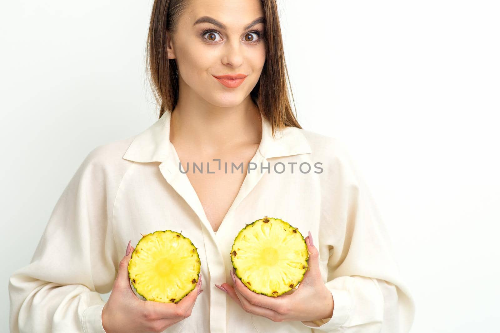 Young Caucasian smiling woman holding slices pineapple over white background, breast health concept
