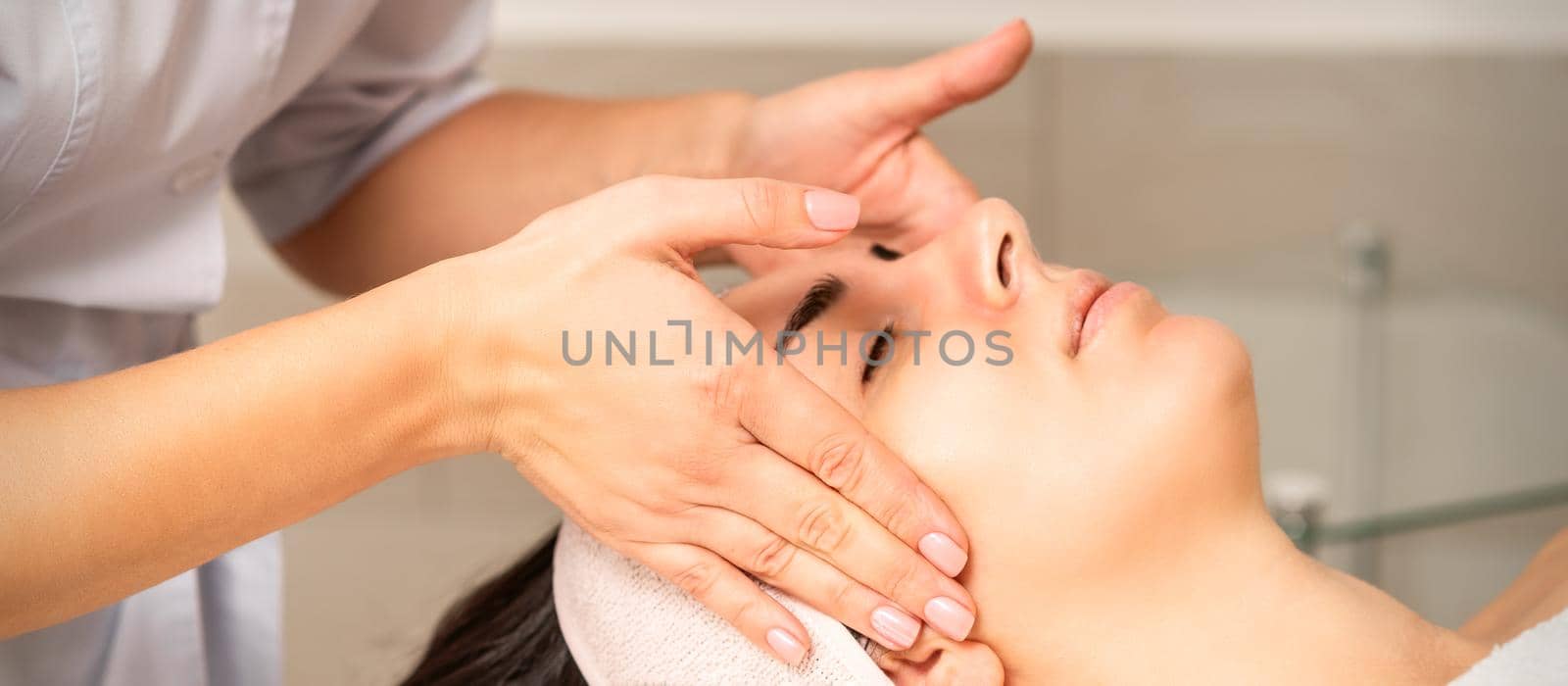 Young caucasian woman with closed eyes getting a facial massage in a beauty clinic. by okskukuruza