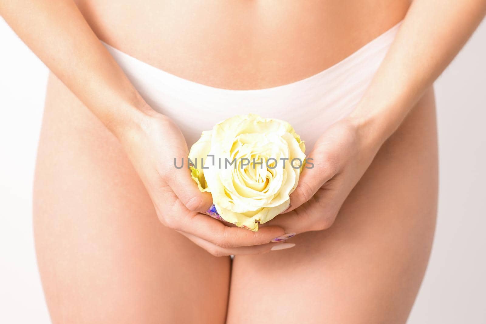 Caucasian woman in white panties with white rose flower on a uniform background, closeup