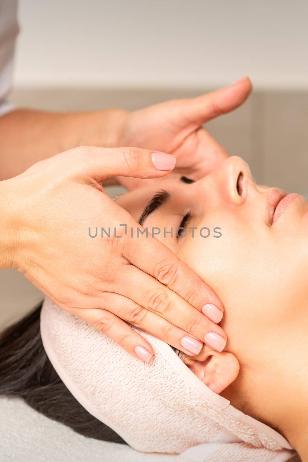 Young caucasian woman with closed eyes getting a facial massage in a beauty clinic. by okskukuruza