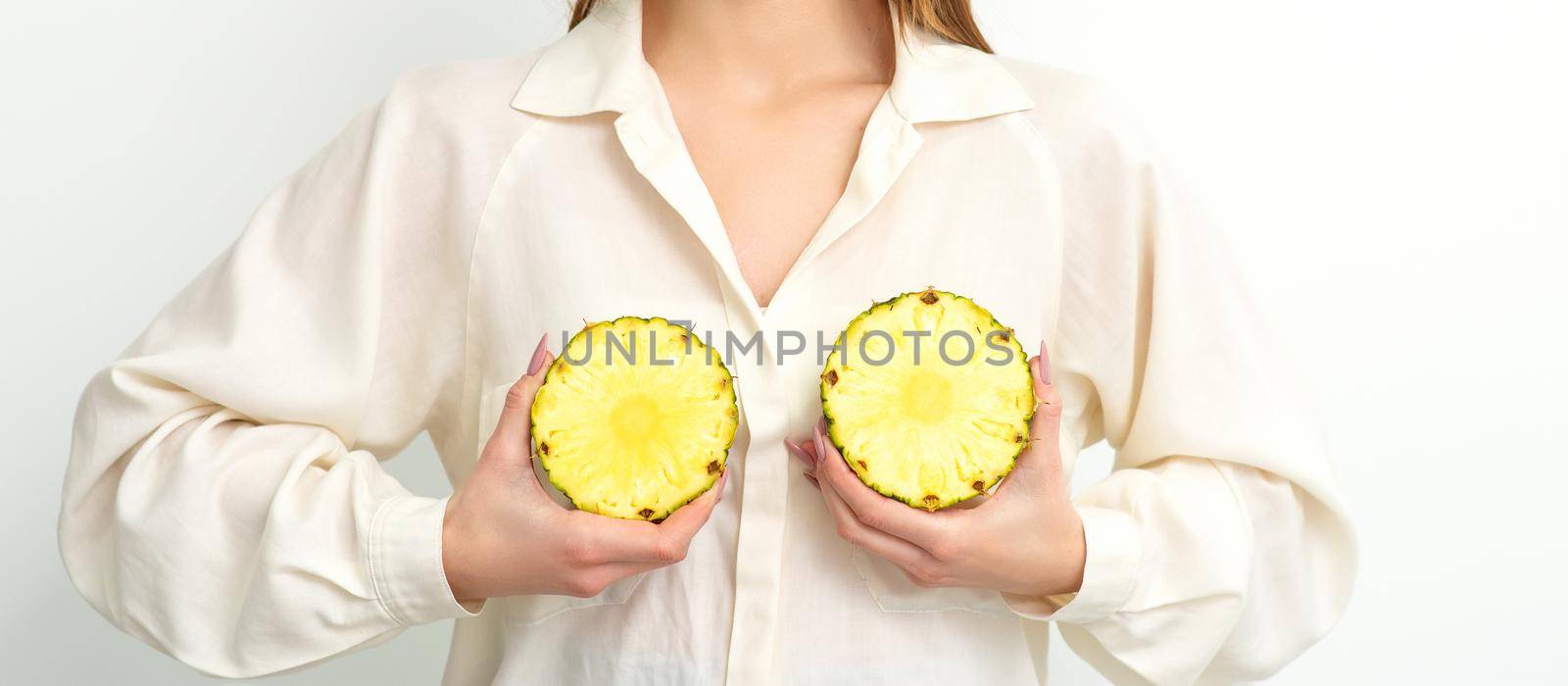 Young Caucasian smiling woman holding slices pineapple over white background, breast health concept. by okskukuruza