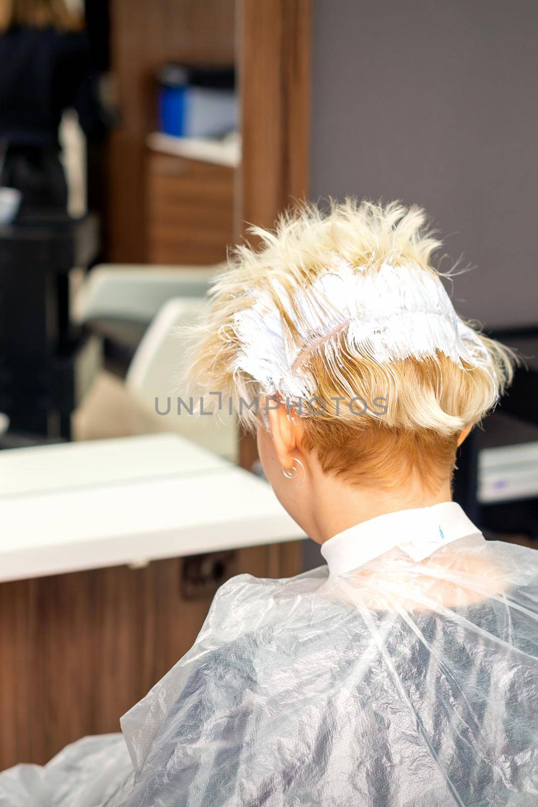 Coloring white hair with hair dye of the young caucasian blonde woman sitting at a hair salon, close up. by okskukuruza