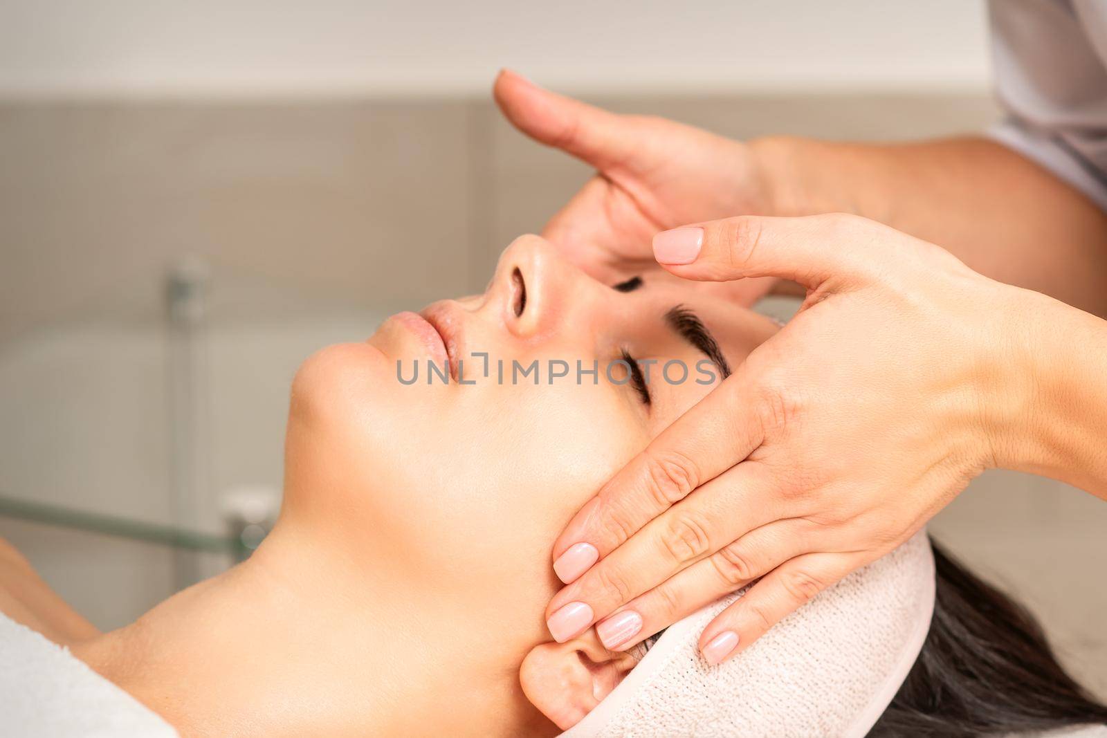 Young caucasian woman with closed eyes getting a facial massage in a beauty clinic