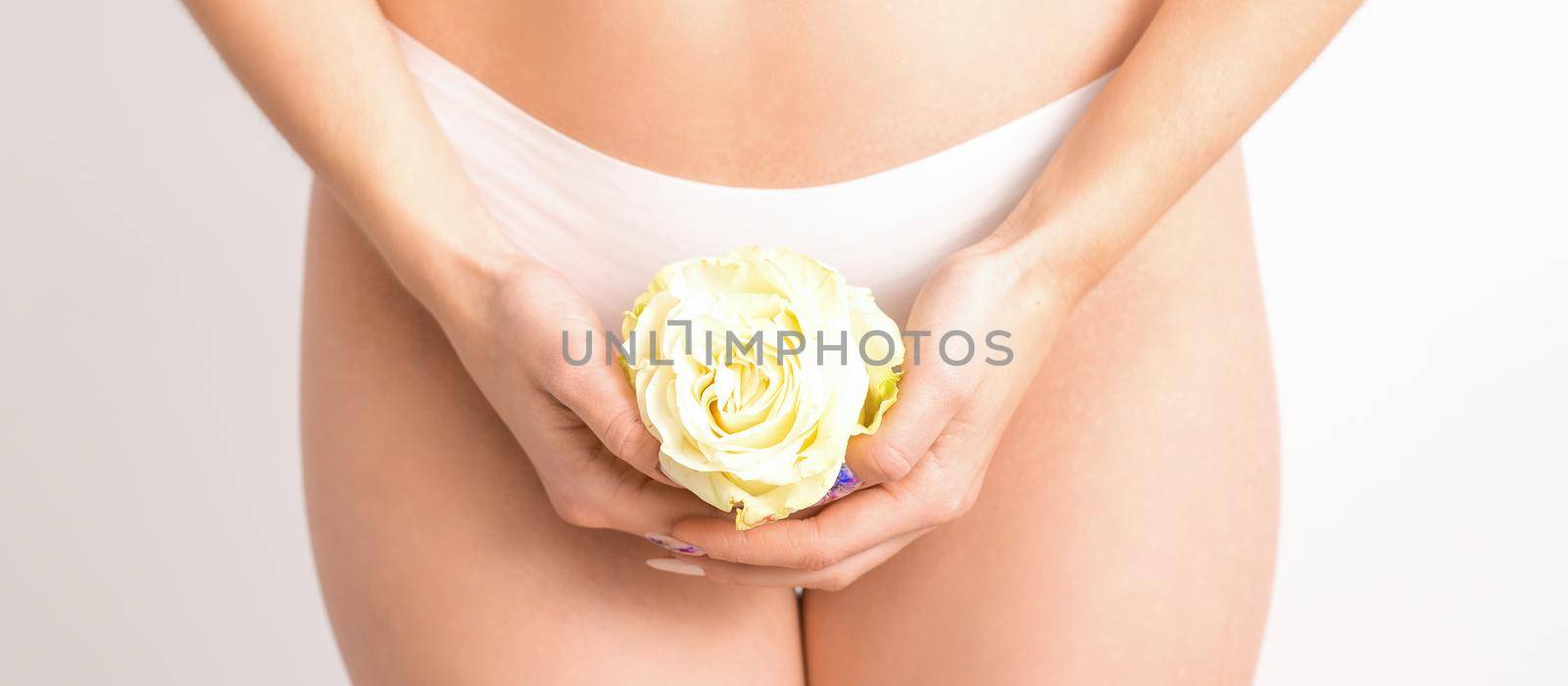 Caucasian woman in white panties with white rose flower on a uniform background, closeup