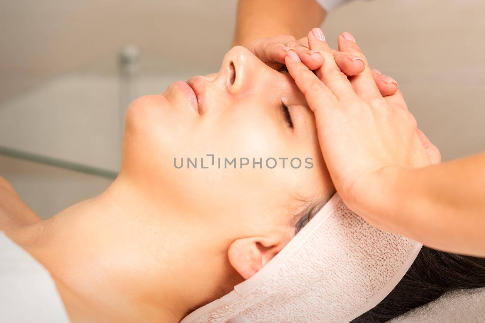 Facial massage. Young caucasian woman with closed eyes getting a massage on her forehead in a beauty salon. by okskukuruza