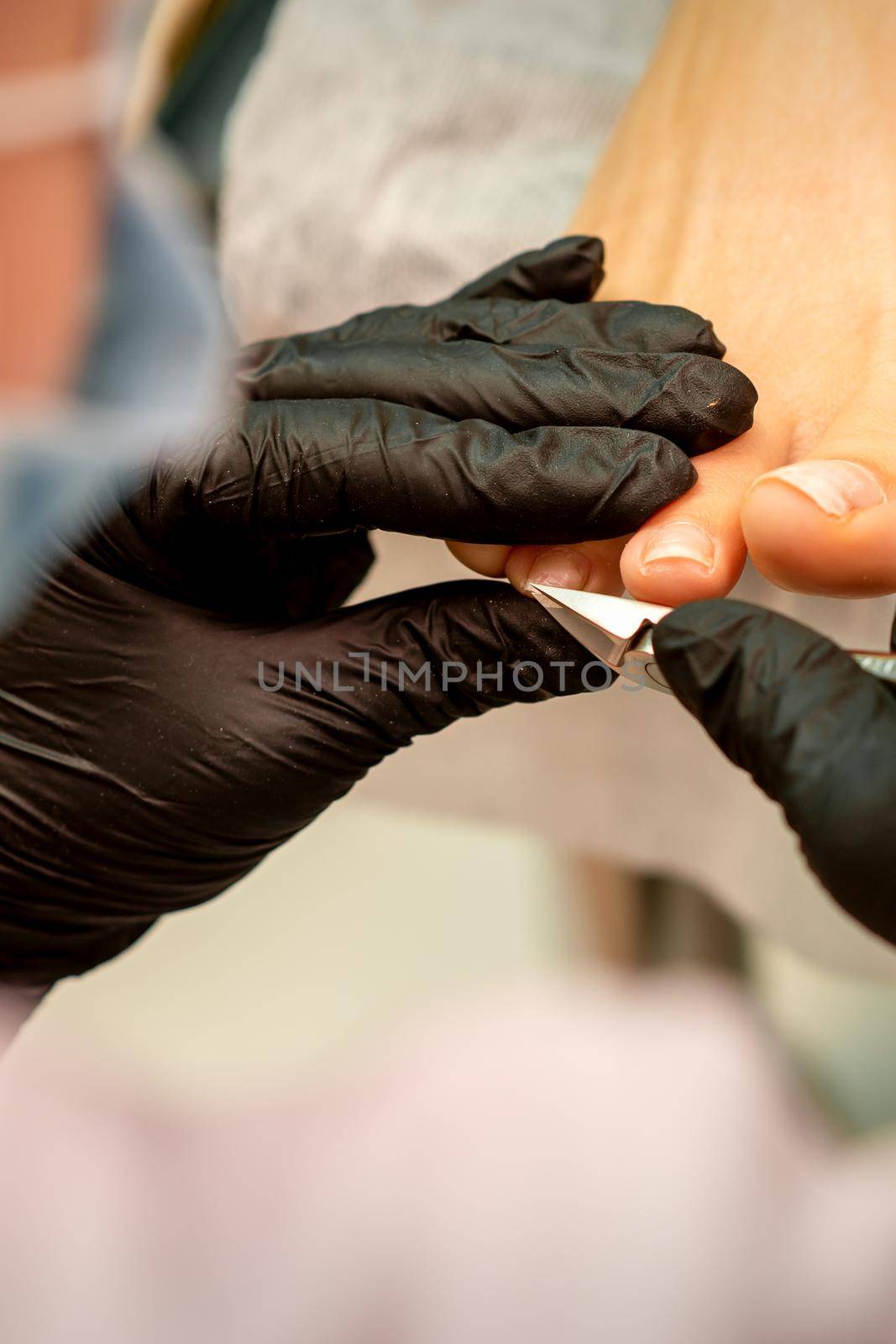 Professional pedicure. Pedicure master wearing latex gloves cuts female toenails in the beauty salon, closeup