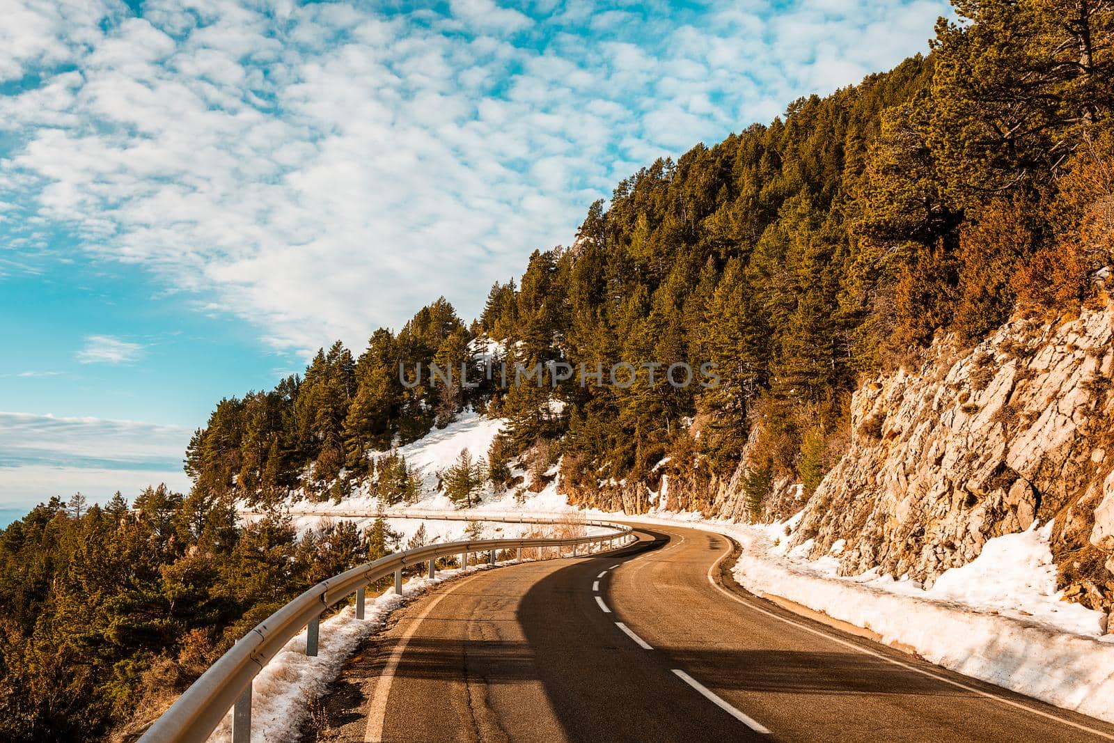 winding road in the mountains with snow in the gutter is lost in the distance, the road is surrounded by forests and the sky is clear
