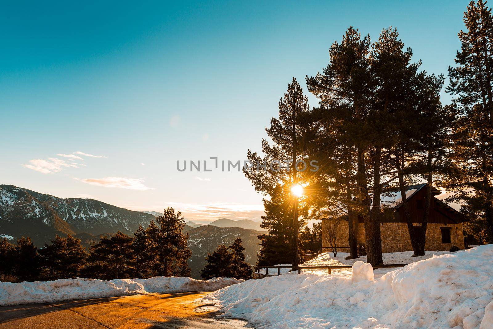 cabin among the trees covered in snow, dawns in the mountains in the background