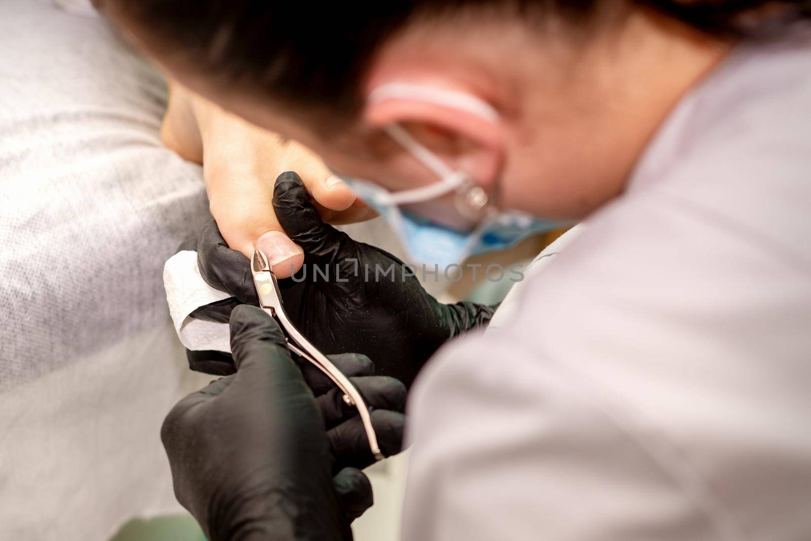 Professional pedicure. Pedicure master wearing latex gloves cuts female toenails in the beauty salon, closeup