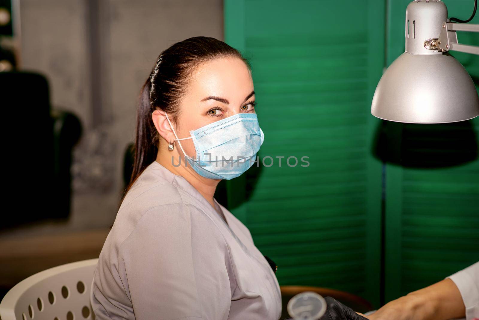 Young female podiatrist with a protective mask looking at the camera in her podiatry clinic. by okskukuruza