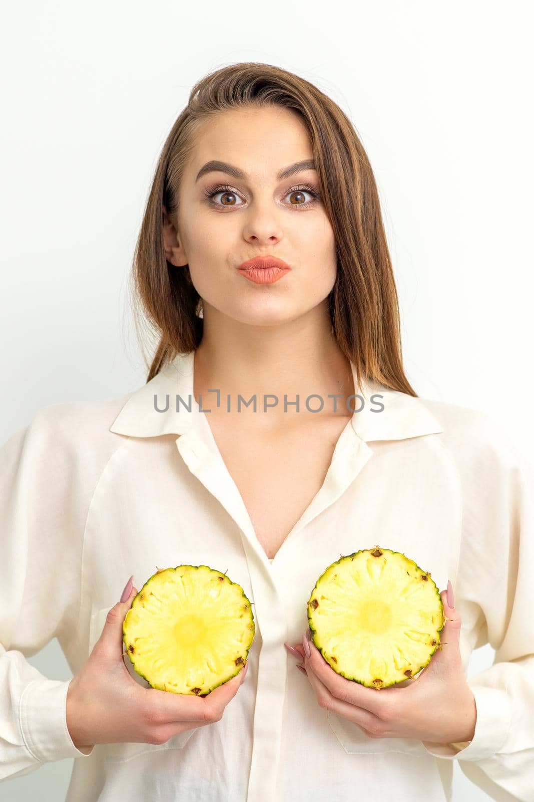 Young Caucasian smiling woman holding slices pineapple over white background, breast health concept