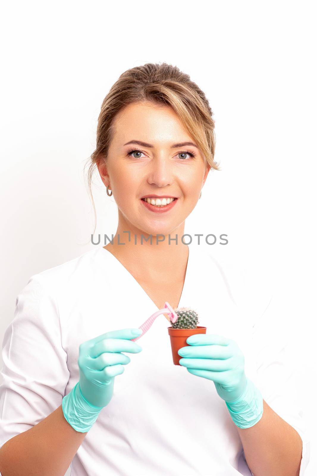 A smiling female beautician holds little green cactus with the razor in her hands. Hair removal concept