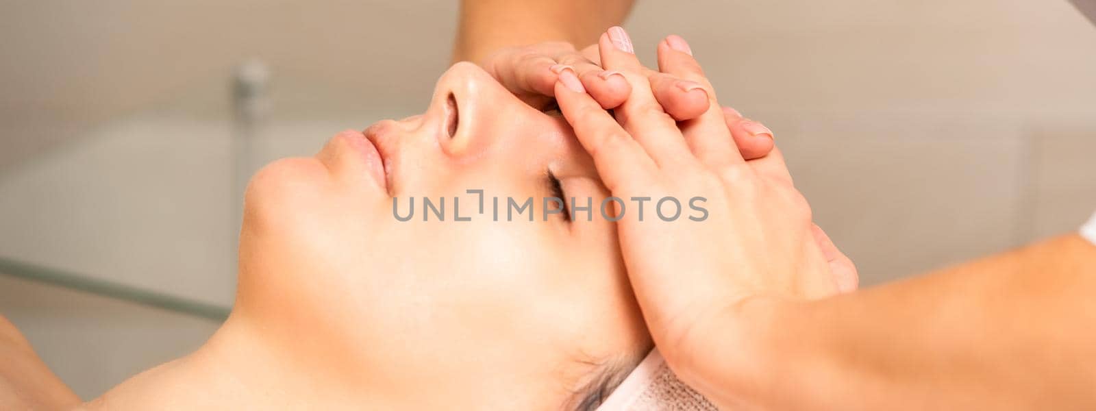 Facial massage. Young caucasian woman with closed eyes getting a massage on her forehead in a beauty salon