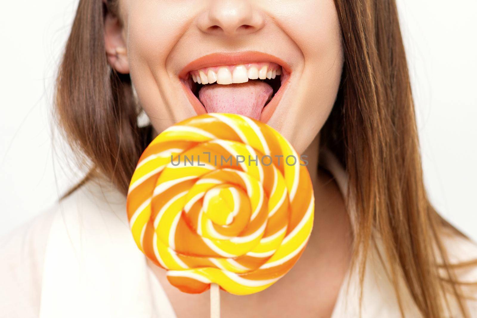 Beautiful young caucasian woman wearing a white shirt licking a lollipop on a white background