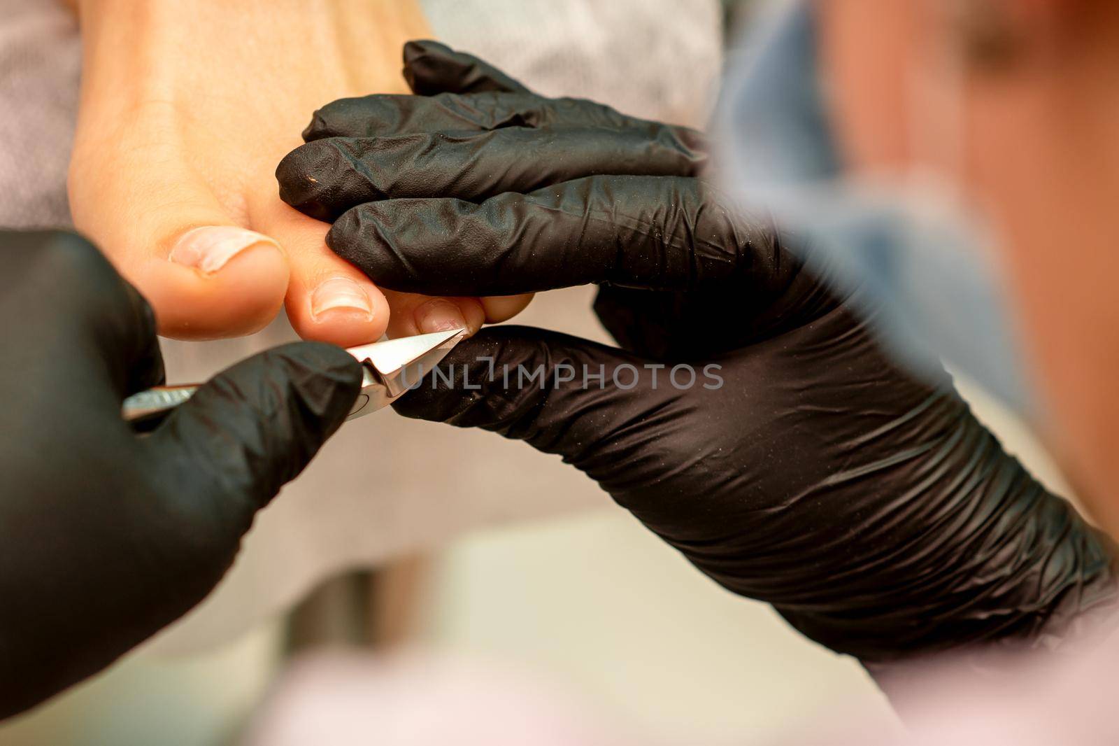 Professional pedicure. Pedicure master wearing latex gloves cuts female toenails in the beauty salon, closeup