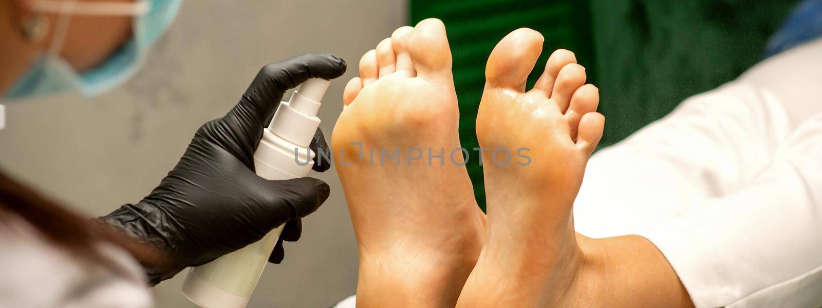 A woman getting a pedicure and pedicurist moisturizing female feet with lotion spraying in a beauty salon