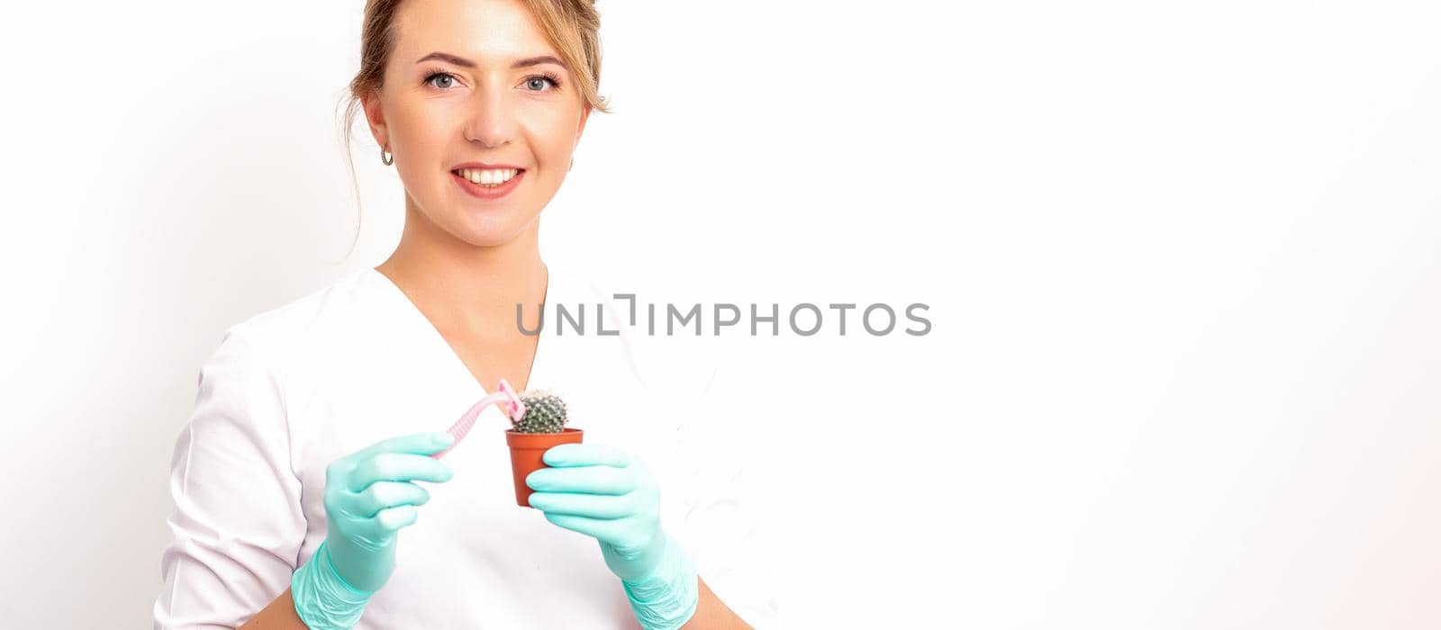 A smiling female beautician holds little green cactus with the razor in her hands. Hair removal concept