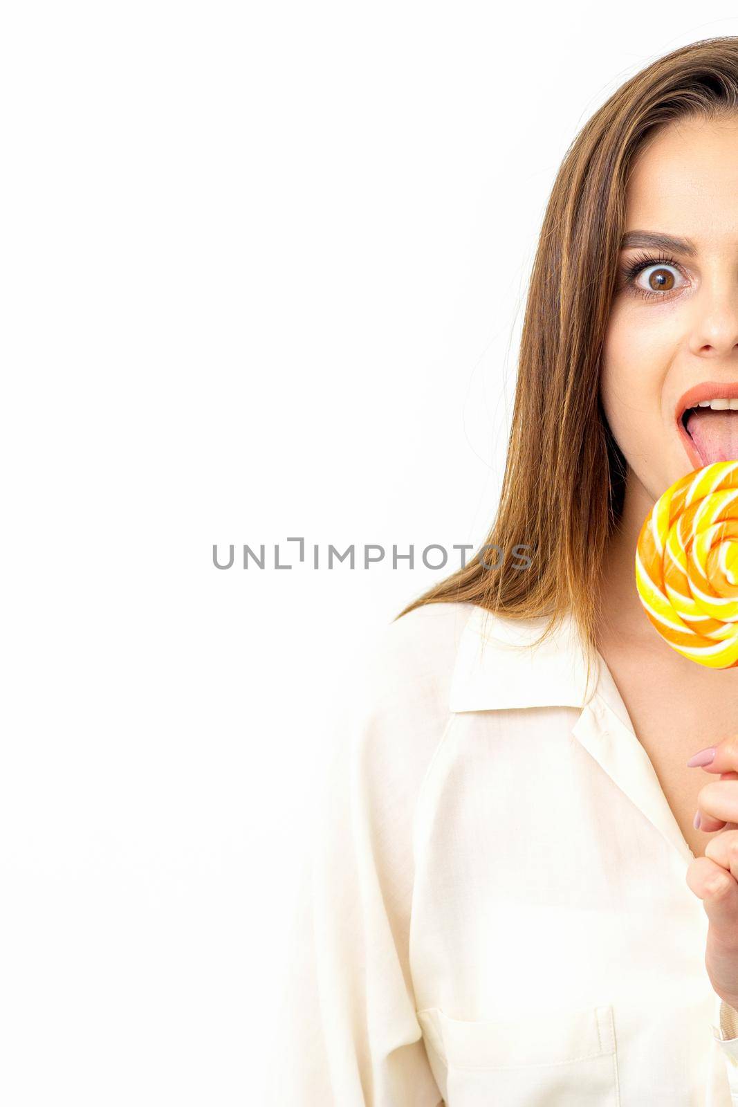 Beautiful young caucasian woman wearing a white shirt licking a lollipop on a white background. by okskukuruza