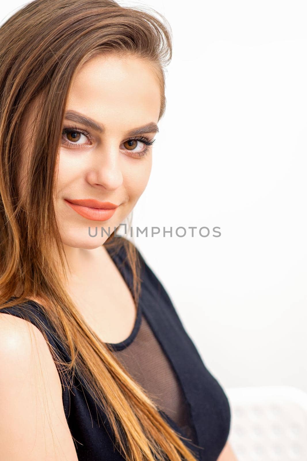 Portrait of a beautiful young caucasian smiling brunette woman with long straight hair standing and looking at the camera on white background