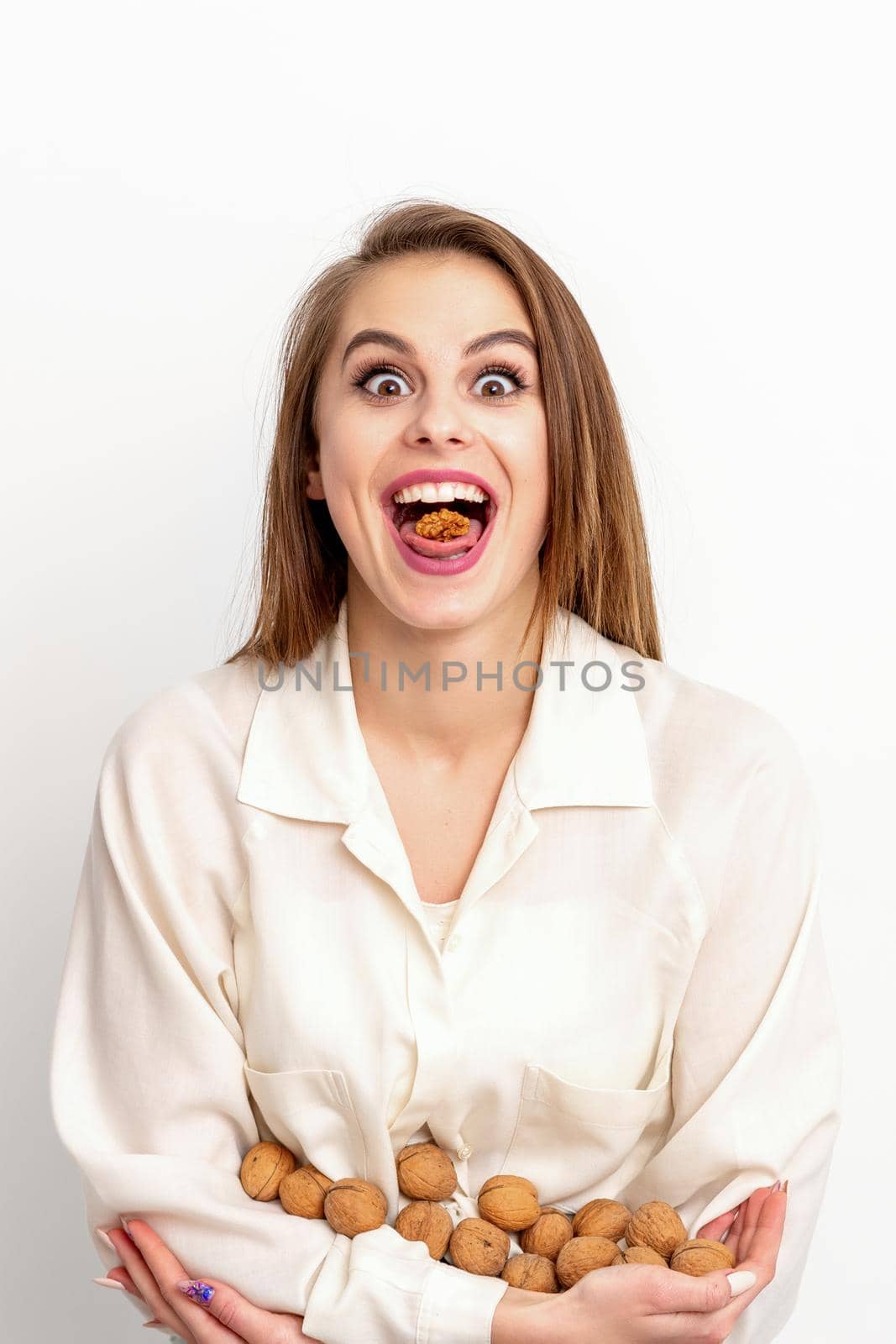 Happy young caucasian woman eating walnuts with an open mouth on white background with copy space