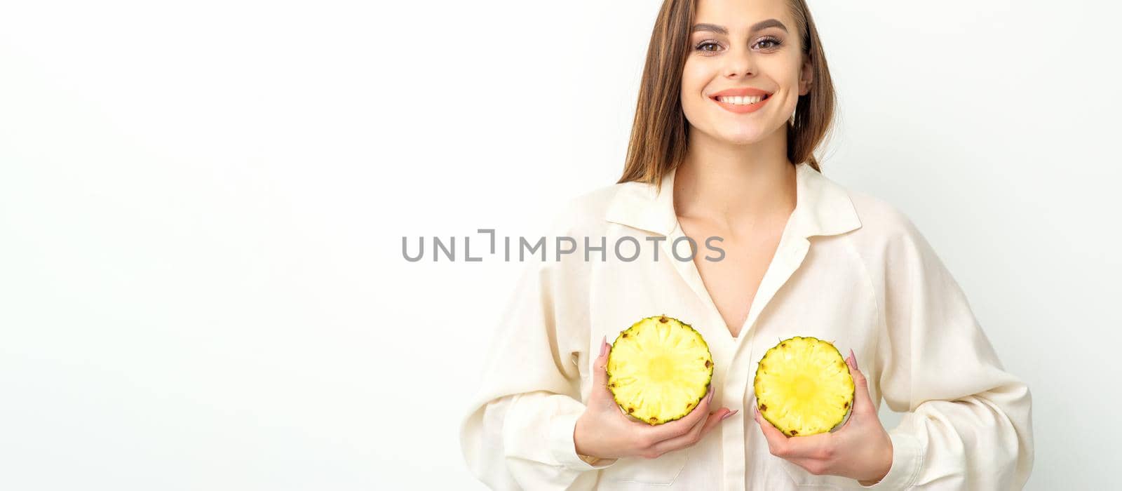 Young Caucasian smiling woman holding slices pineapple over white background, breast health concept. by okskukuruza