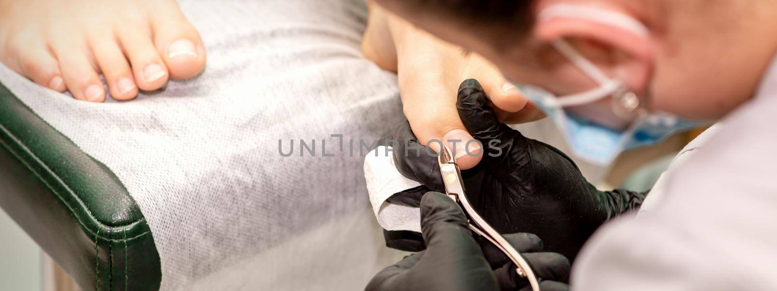 Professional pedicure. Pedicure master wearing latex gloves cuts female toenails in the beauty salon, closeup