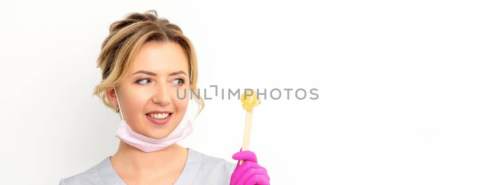 The master of sugar hair removal holds liquid yellow sugar paste, wax for depilation on a wooden stick on a white background