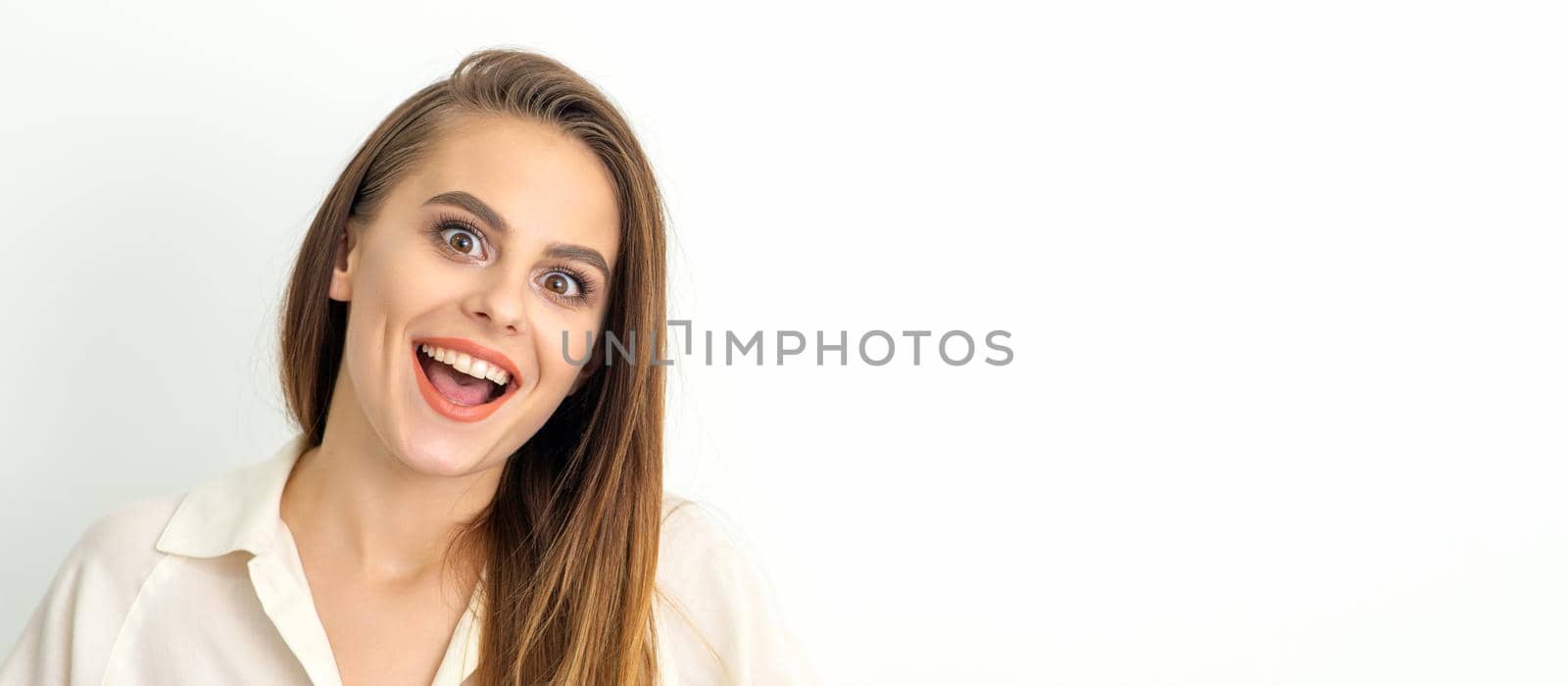 Portrait of a young caucasian happy woman wearing white shirt smiling with open mouth against the white background. by okskukuruza