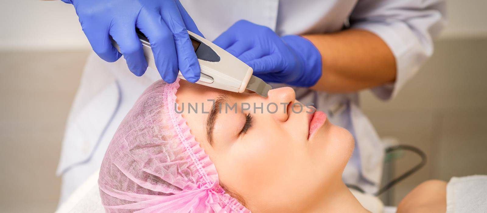 Young caucasian woman receiving facial skin cleaning by ultrasonic cosmetology face equipment in a medical salon. by okskukuruza