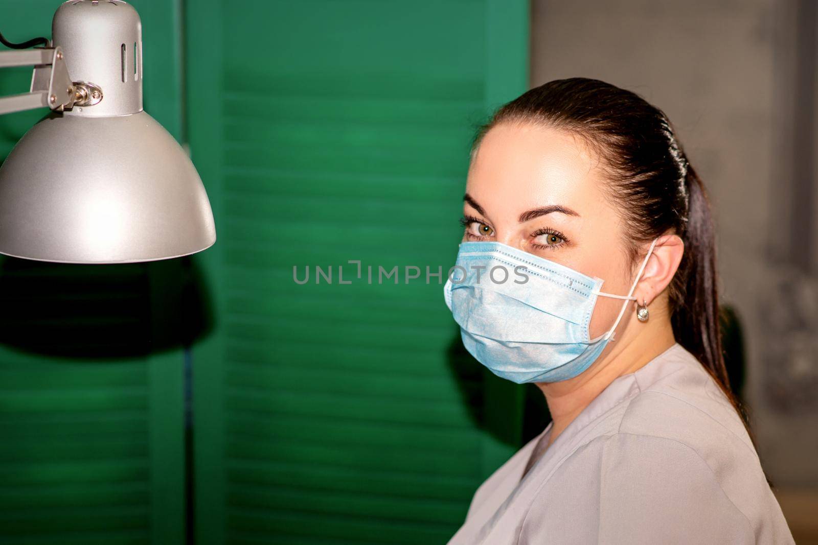 Young female podiatrist with a protective mask looking at the camera in her podiatry clinic. by okskukuruza