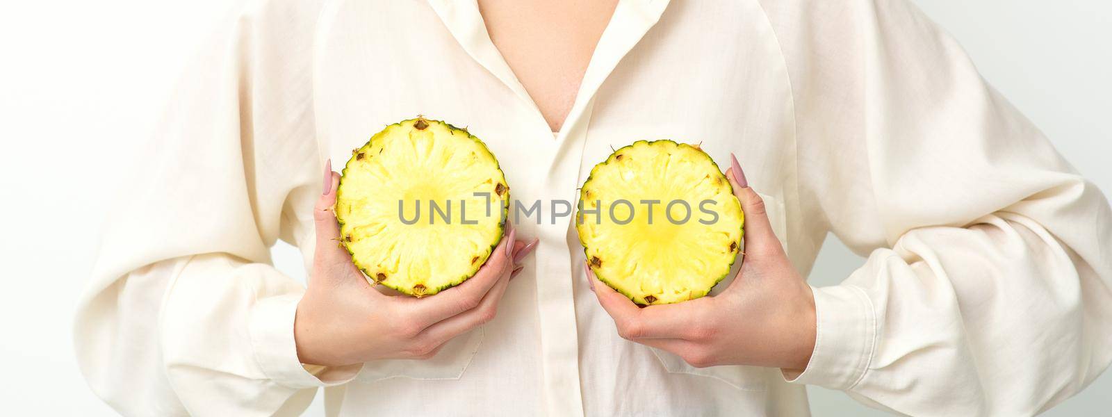 Young Caucasian smiling woman holding slices pineapple over white background, breast health concept