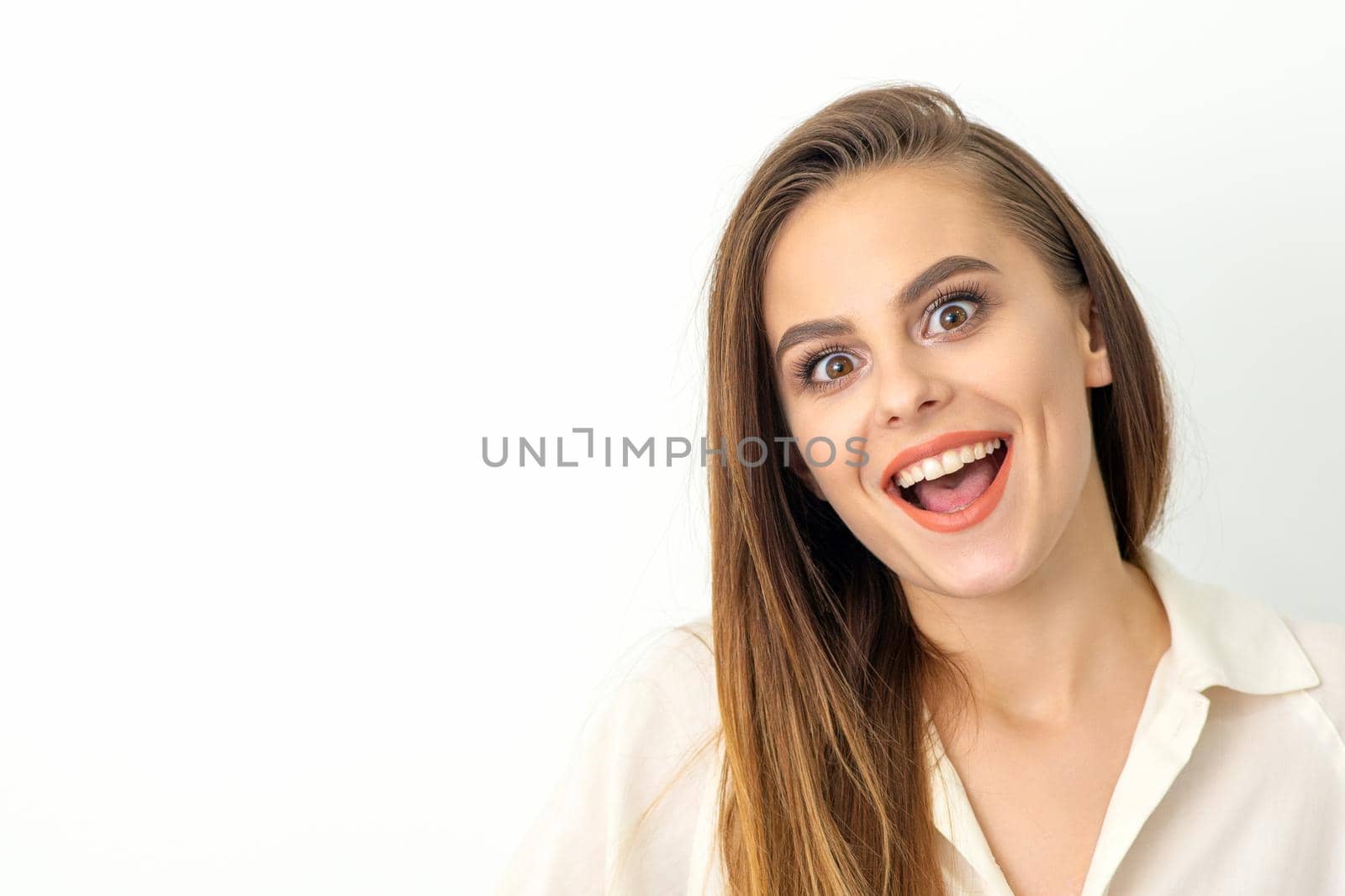 Portrait of a young caucasian happy woman wearing white shirt smiling with open mouth against the white background. by okskukuruza