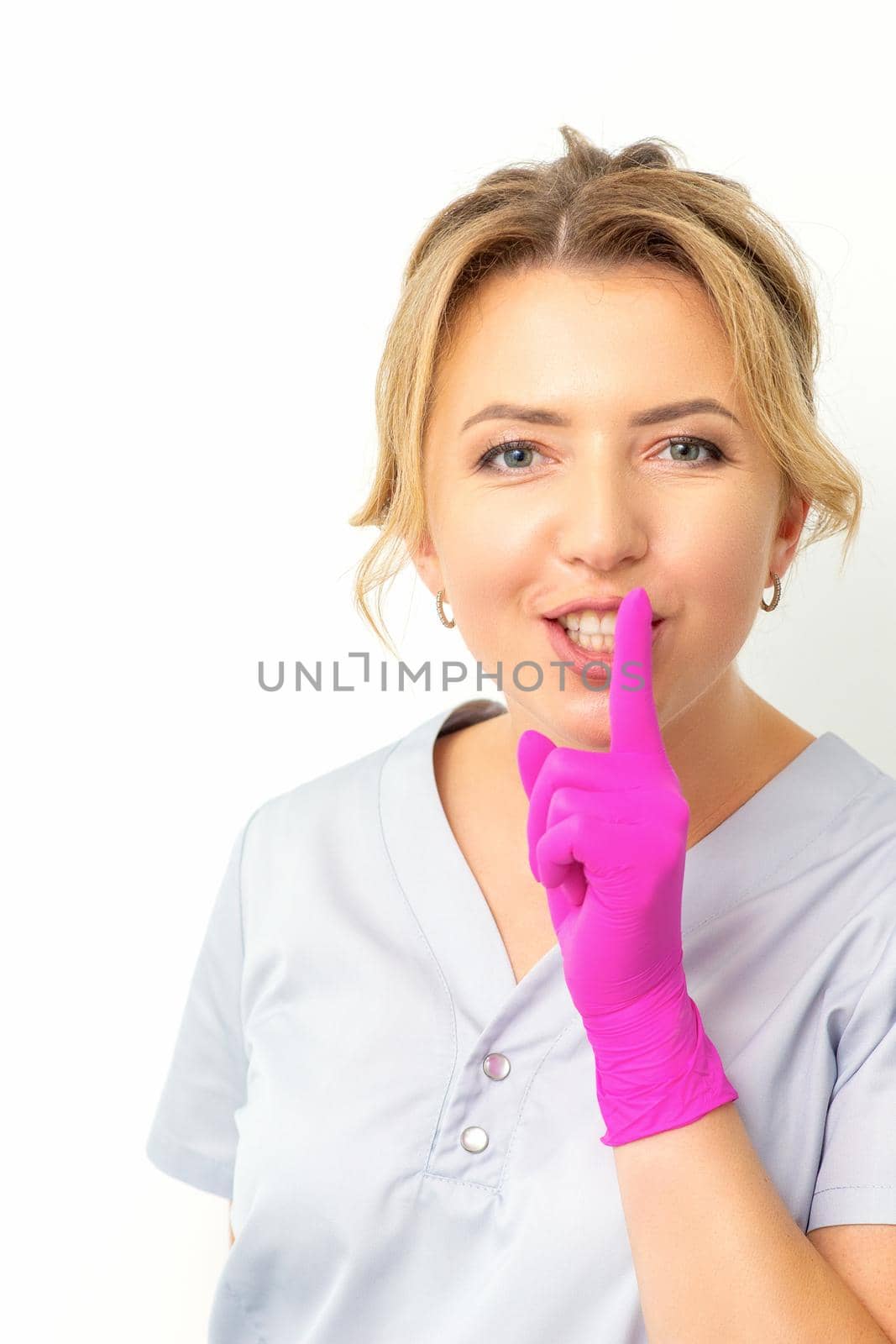 Young beautiful caucasian woman doctor, beautician doing silent gesture pressing his index finger to his lips isolated on white background. by okskukuruza