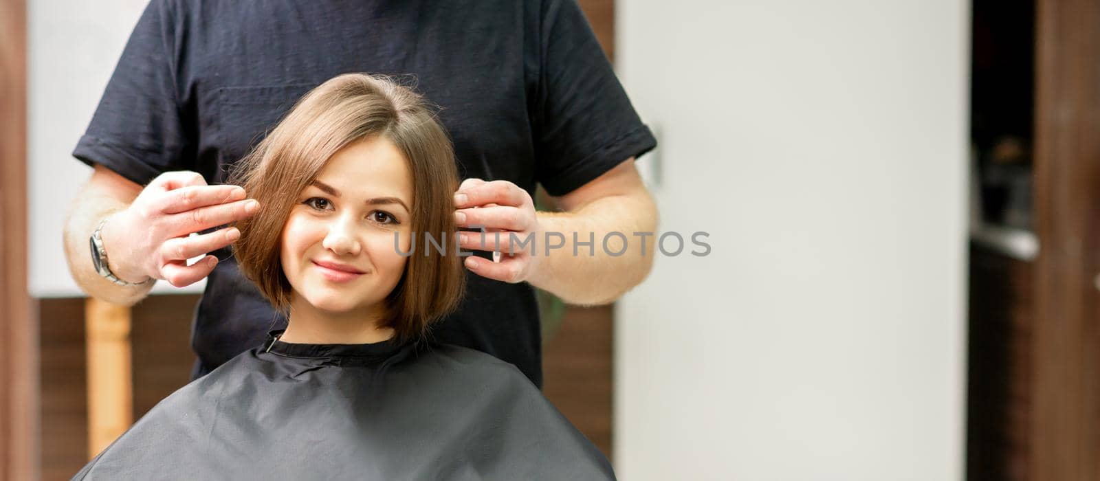Gorgeous brunette short hair woman and her male hairdresser looking and checking out hairstyle. Beautiful hairstyle of a young brunette woman, results of hair treatment in a beauty salon