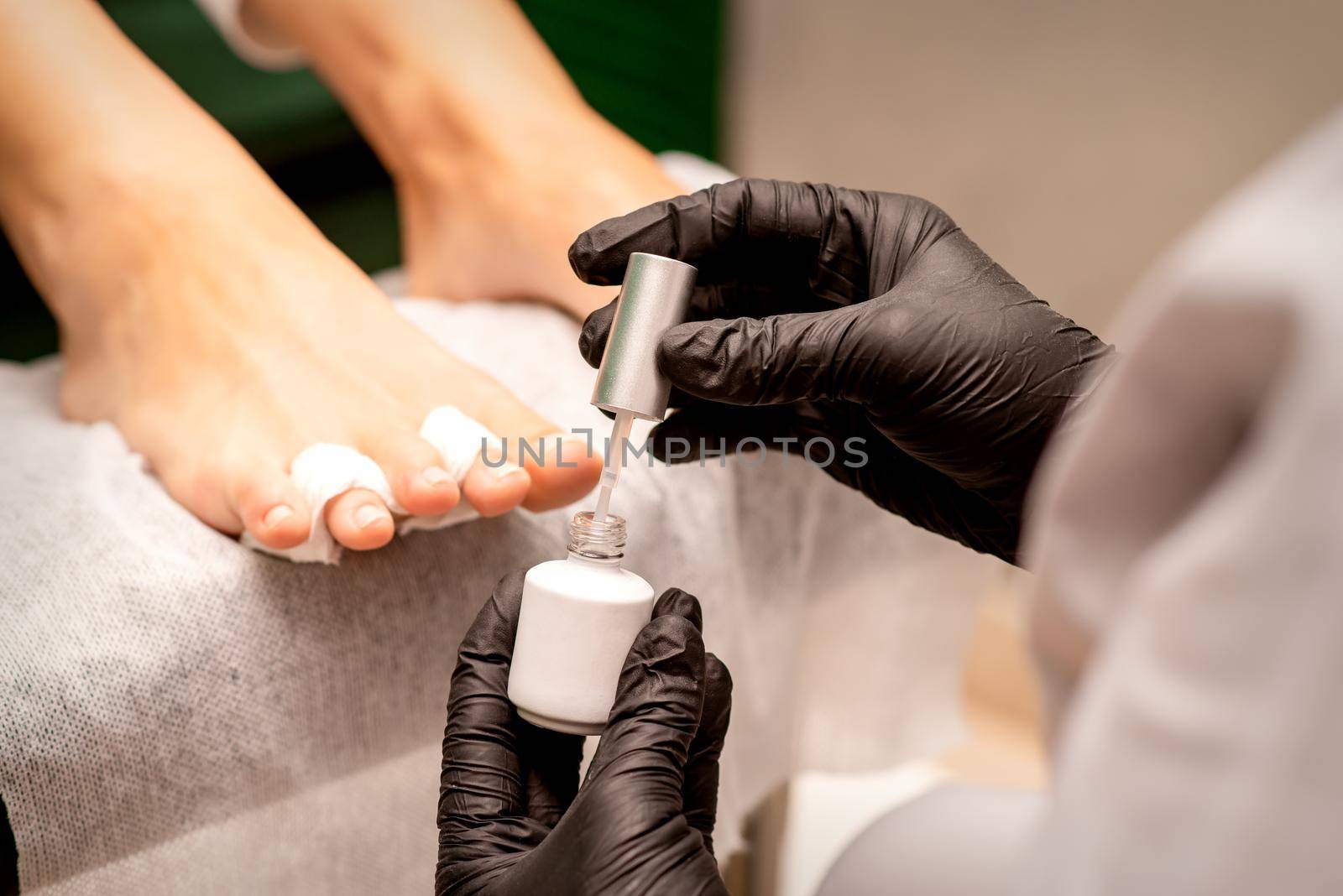 White nail polish in the hands of a manicurist while painting nails on a female feet, closeup