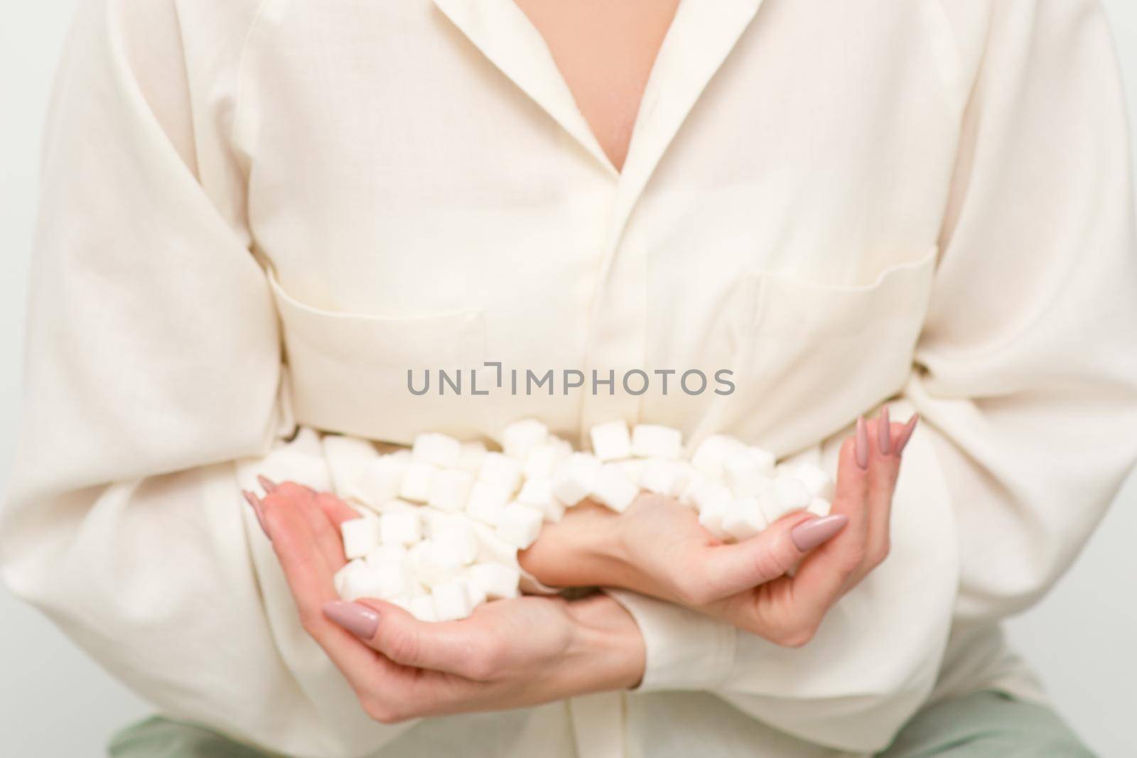 Portrait of young caucasian woman holding sugar cubes heap standing and looking at the camera against a white background. by okskukuruza