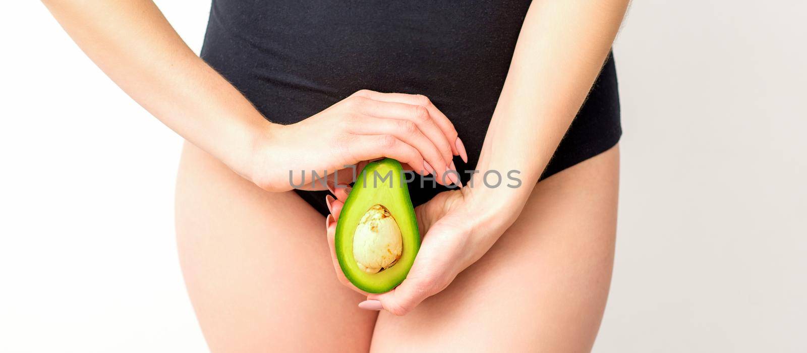 Healthy nutrition and pregnancy concept. Young woman holding one half of an avocado fruit close to her belly over a white background