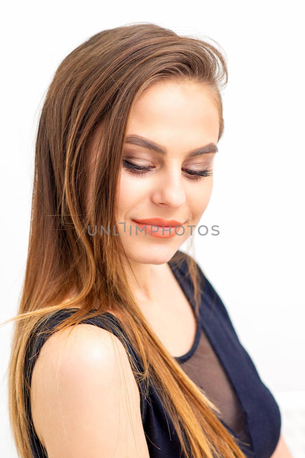 Portrait of a beautiful young caucasian smiling brunette woman with long straight hair standing and looking down on white background