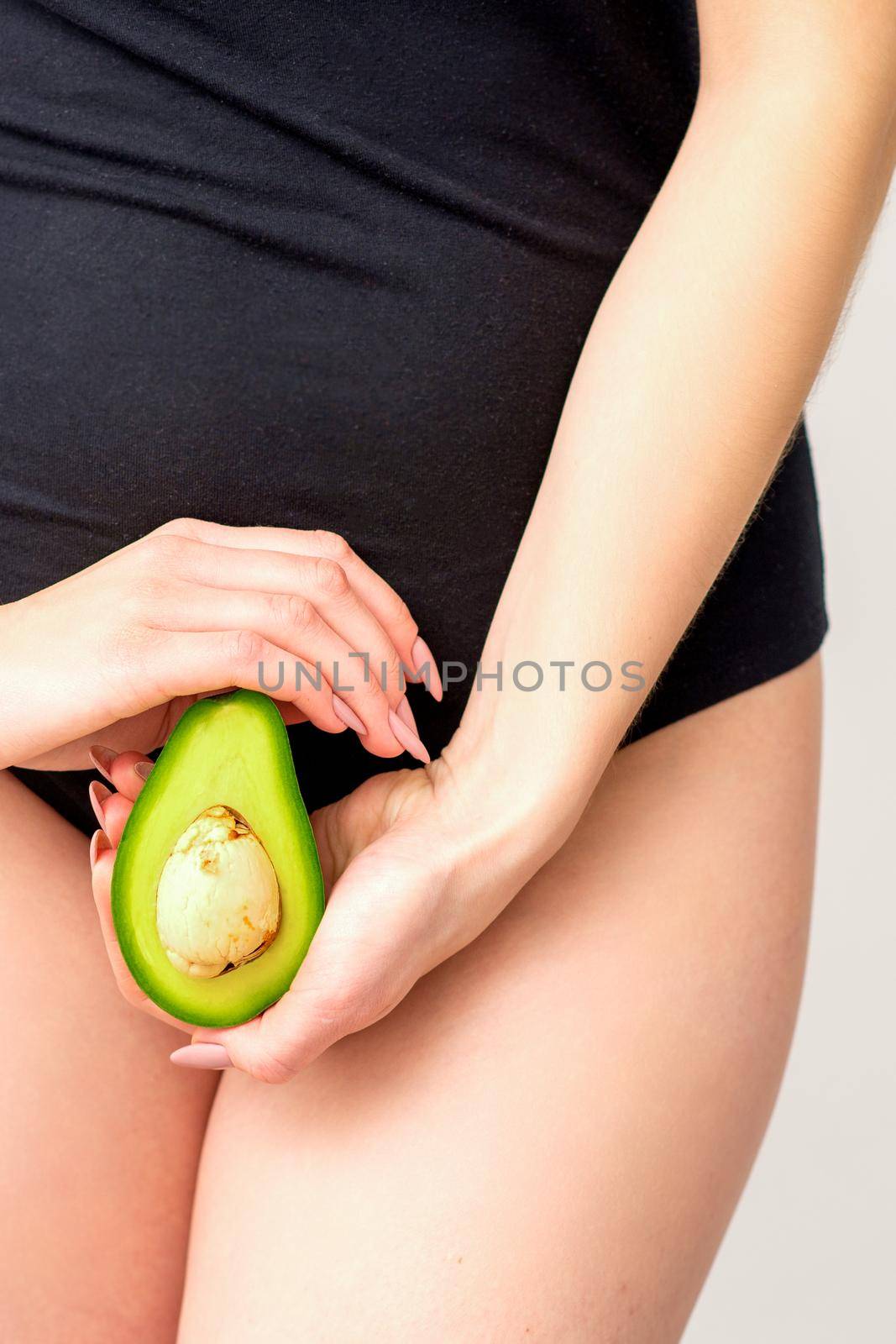 Healthy nutrition and pregnancy concept. Young woman holding one half of an avocado fruit close to her belly over a white background. by okskukuruza