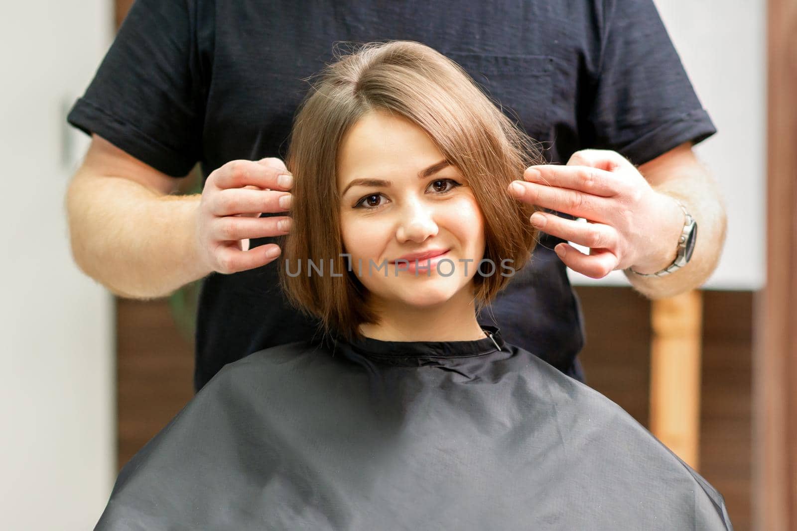 Gorgeous brunette short hair woman and her male hairdresser looking and checking out hairstyle. Beautiful hairstyle of a young brunette woman, results of hair treatment in a beauty salon