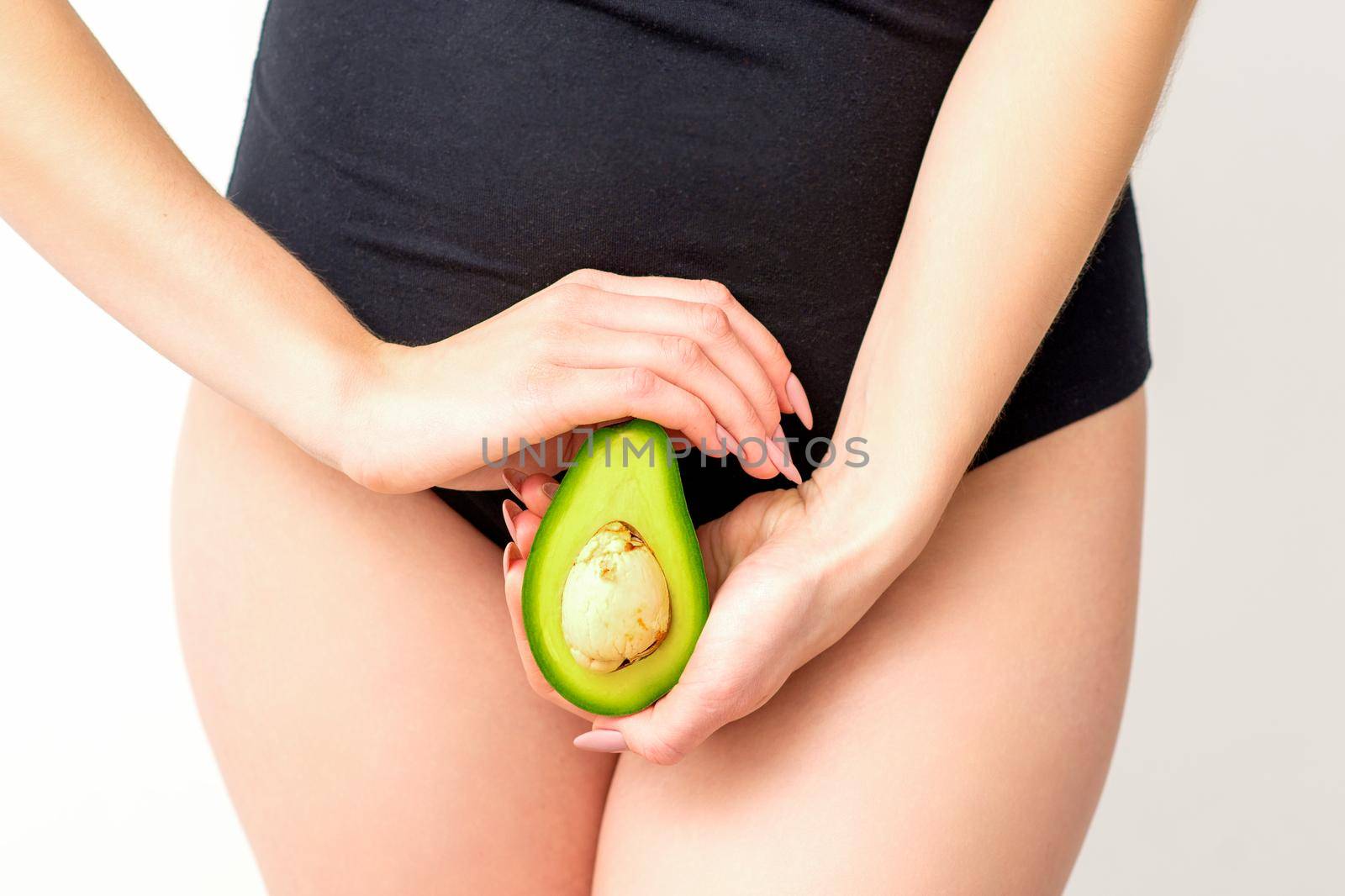 Healthy nutrition and pregnancy concept. Young woman holding one half of an avocado fruit close to her belly over a white background