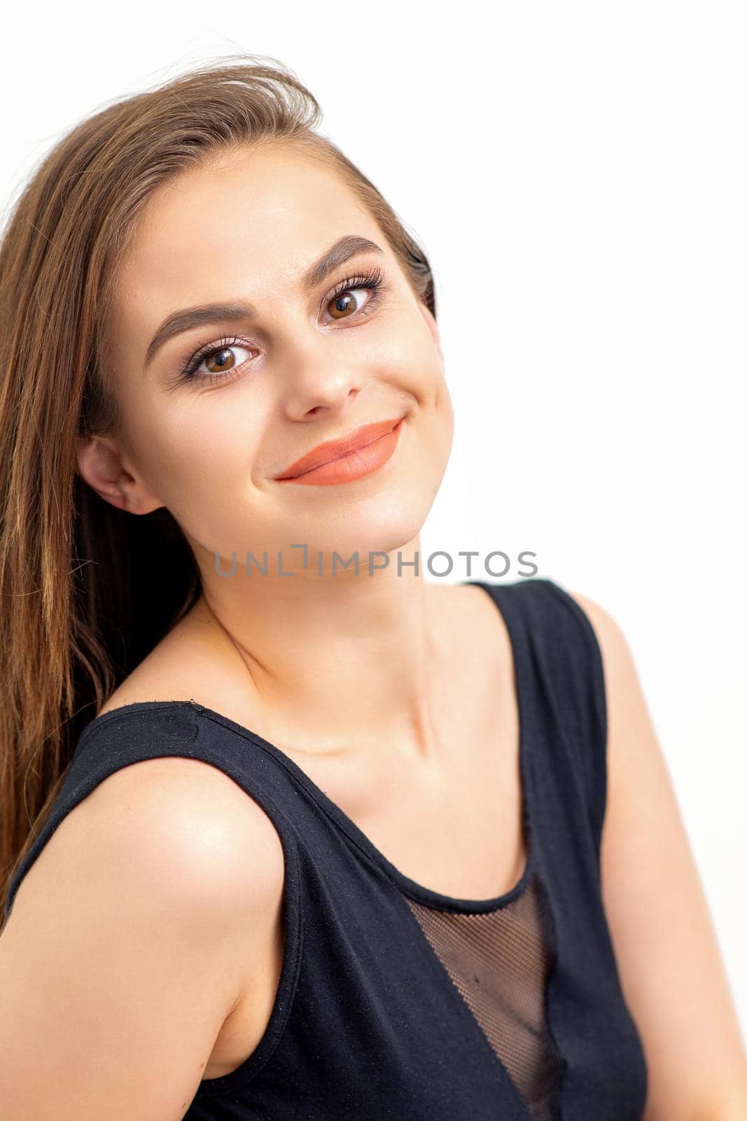 Portrait of a beautiful young caucasian smiling brunette woman with long straight hair standing and looking at the camera on white background. by okskukuruza