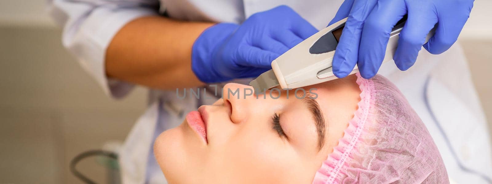 Young caucasian woman receiving facial skin cleaning by ultrasonic cosmetology face equipment in a medical salon. by okskukuruza